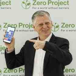 Man standing in front of a logo wall and pointing at his smartphone