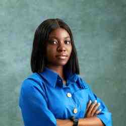 Headshot of Confidence Awak, Ashoka Africa Staff. Person with dark shoulder length hair and a blue blouse smiling at the camera slight profile right. Background is dark green