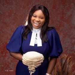 Headshot of Nnenna Isu Omo, Ashoka Africa staff. Person with shoulder length black hair and brown skin dressed in blue dress smiling at the camera, background is dark brown.