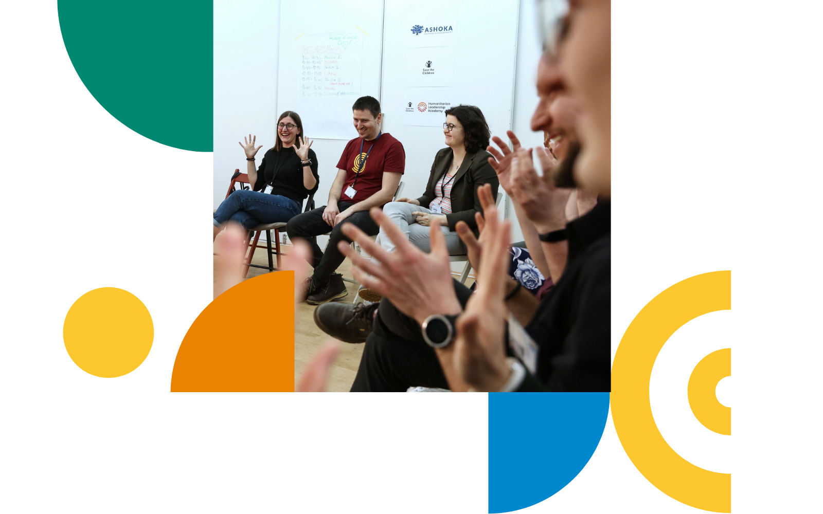 Participants sit in a circle during a workshop in a bright meeting room. Several people are raising their hands and smile. The photo is framed by colorful geometric shapes in green, yellow, orange, and blue.