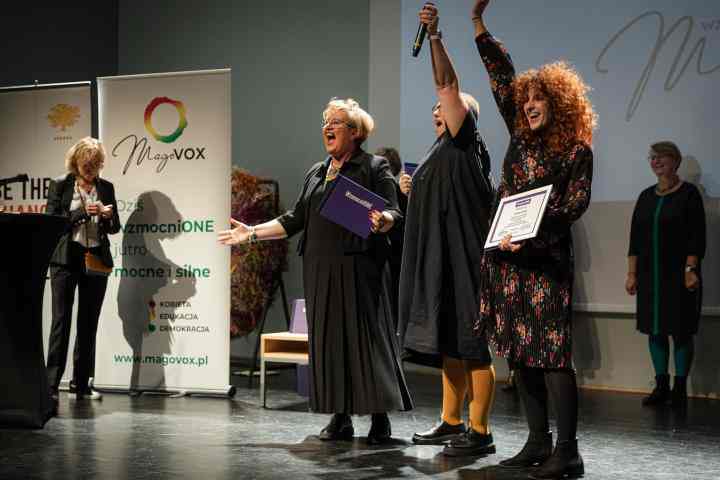 Zdjęcie przedstawia 3 członkinie Fundacji Oficyna-ToTutaj na scenie. Dwie podnoszą ręce w geście zwycięstwa, trzecia śmieje się z rozłożonymi rękami. W tle widać baner Ashoki i Magovoxu oraz uśmiechające się osoby z Jury programu.