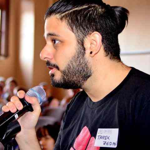 Lebanese man with a beard and a small pony tail holding a mic