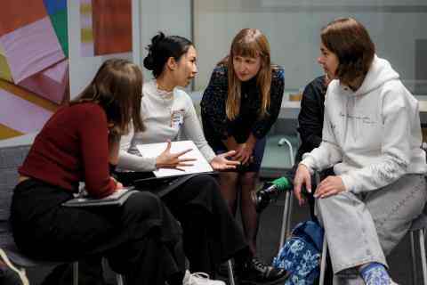 Four young woman sitting on chairs in small circle and talking