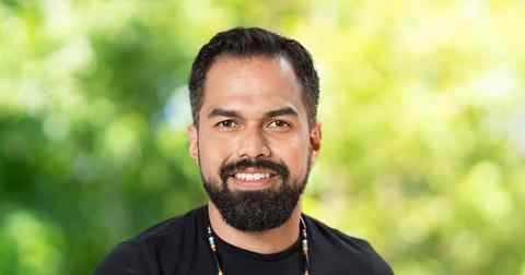 Headshot of Canada Fellow Alejandro Baños. Person with dark short hair, moustache and beard smiling at the camera. dressed in a black top; background of trees