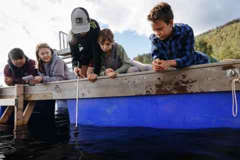Group of youth as well as some parents monitoring water data off the side of a dock