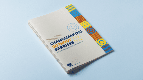 Stack of printed reports titled “Changemaking Without Barriers: Ashoka’s Insights in the Field of Disabilities,” placed on a light blue surface, with a beige cover and a vertical strip of colorful geometric patterns on the right side.