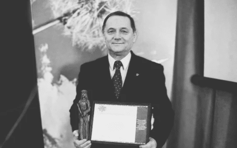 a black and white photo of a man in a suit holding diploma and statuette