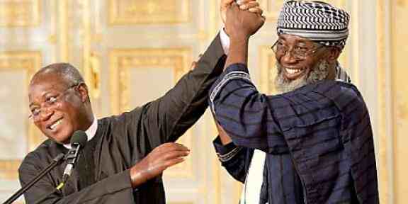 Wspólne zdjęcie pastora Jamesa Wuye i imama Mohammeda Ashafy. Ich złączone ręce są uniesione do góry, obaj się uśmiechają.