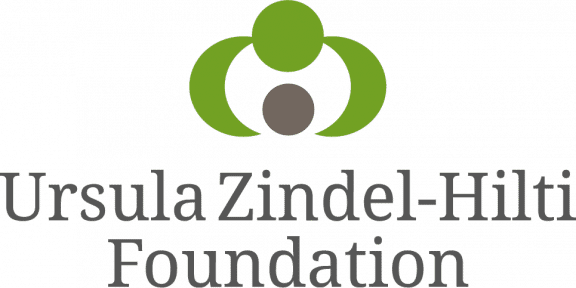 Logo for the Ursula Zindel-Hilti Foundation. One green circle with two half moons also in green coming from both sides downward into space, that leads to another circle that is in grey. Below the words "Ursula Zindel-Hilti Foundation" outlined in grey.