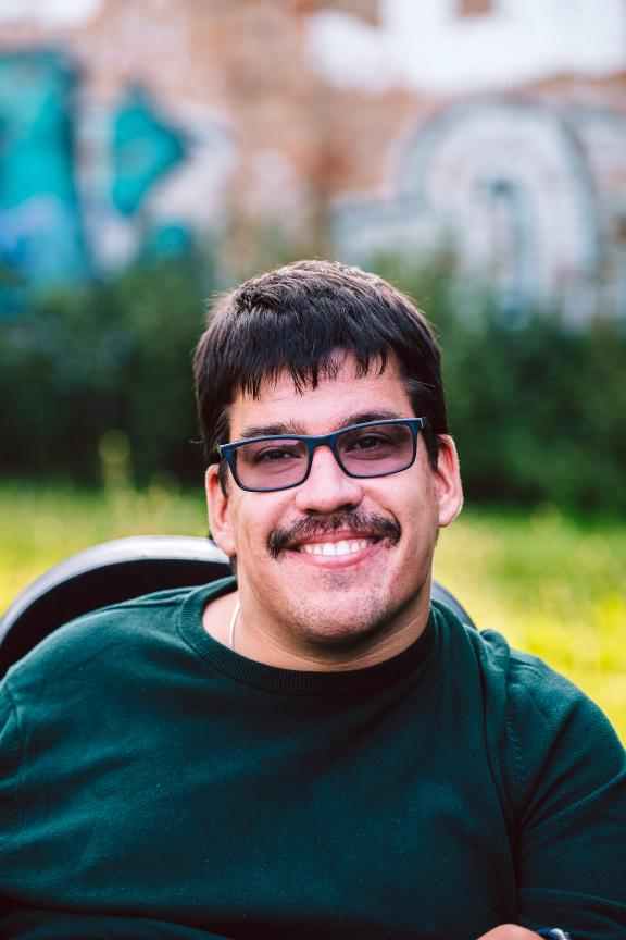 lächelnder Mann mit Brille, Rasen und bemalter Wand im Hintergrund
