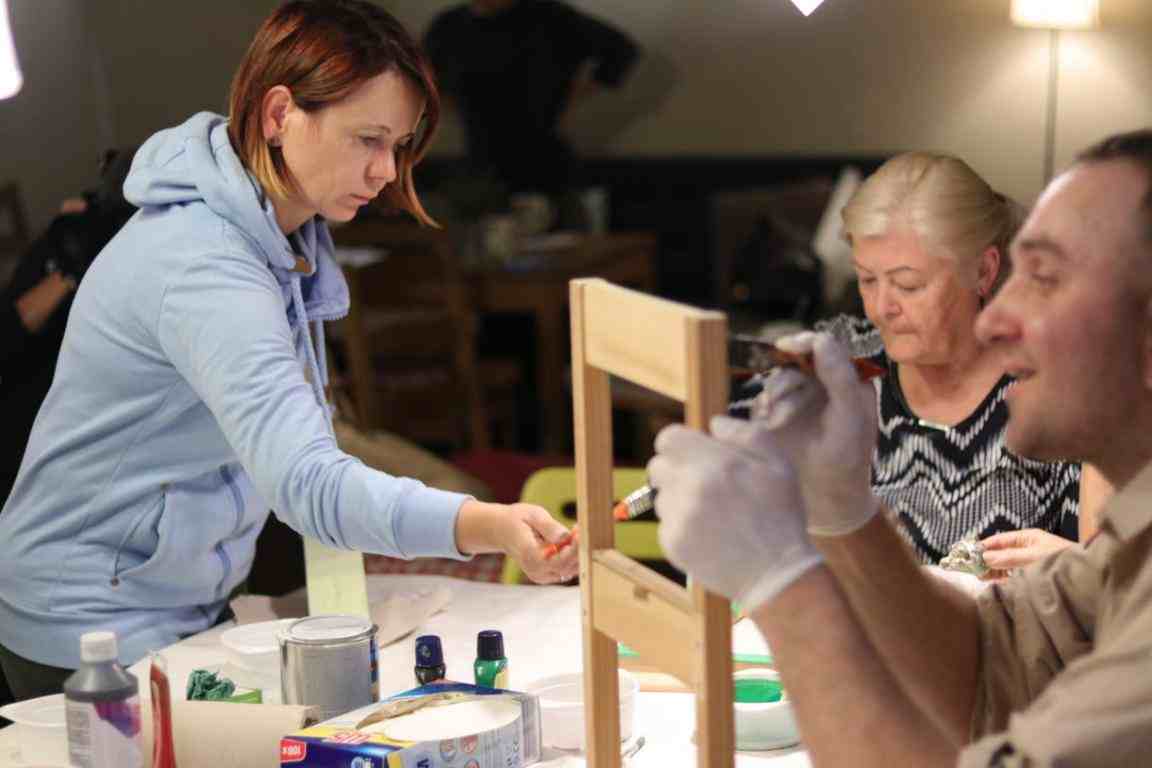 Dwie kobiety oraz mężczyzna wspólnie naprawiają i malują krzesło.