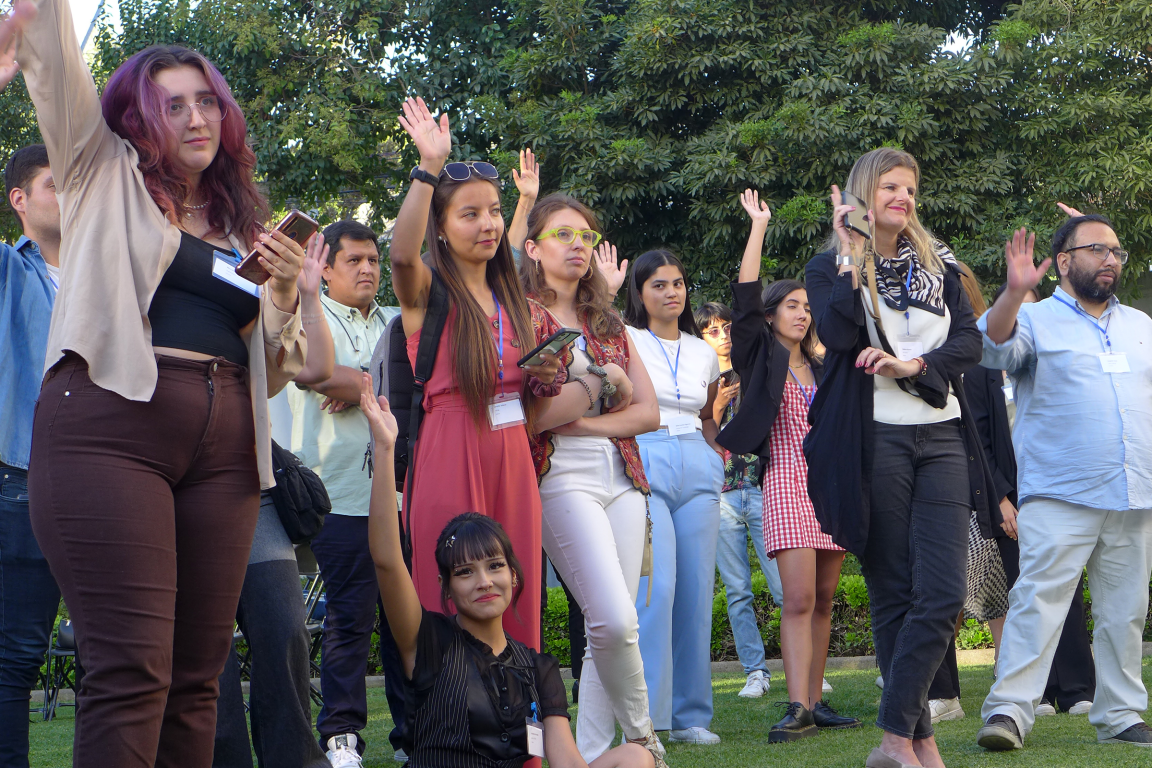 Evento Millones de Jóvenes Agentes de Cambio. Un grupo de personas con la mano alzada mirando hacia adelante. Enfoque de primera fila, jóvenes y adultos mezclados.