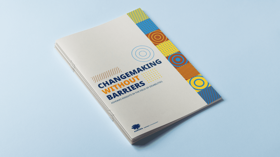 Stack of printed reports titled “Changemaking Without Barriers: Ashoka’s Insights in the Field of Disabilities,” placed on a light blue surface, with a beige cover and a vertical strip of colorful geometric patterns on the right side.