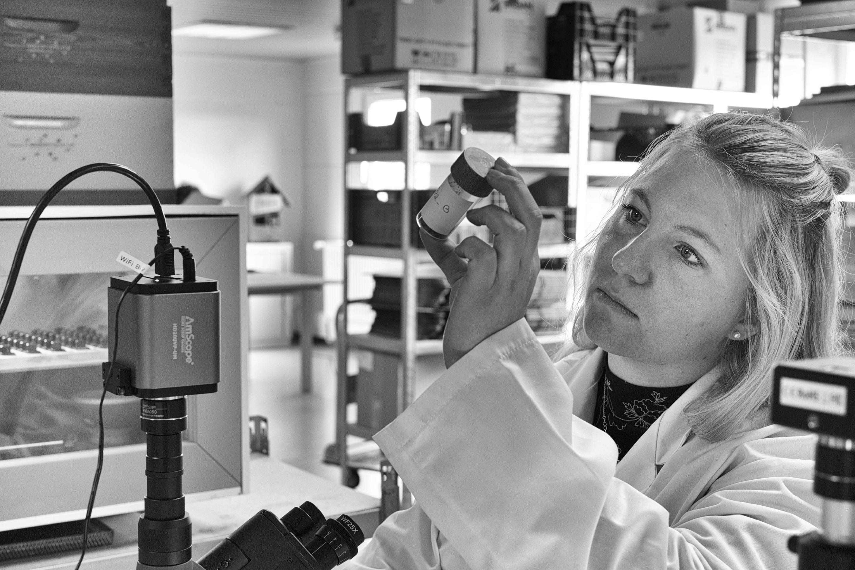 Photo of a person holding up a small bottle in a science lab; black and white photo 