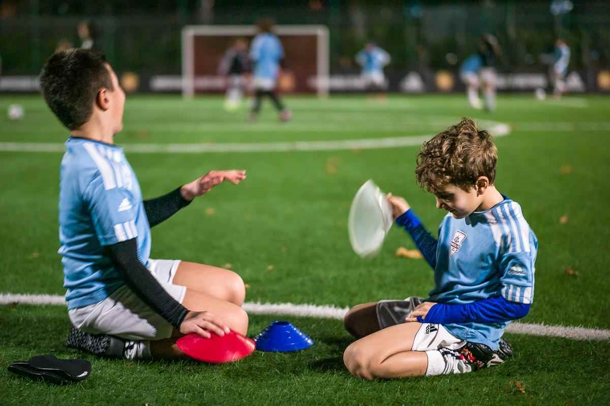 Two children dressed in light blue on the sideline of a futbol field