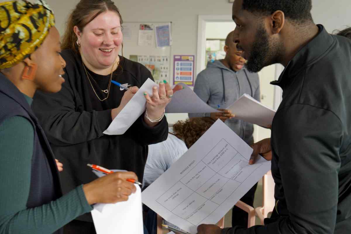 People standing in a circle with paper in their hands, doing a group activity and speaking animatedly