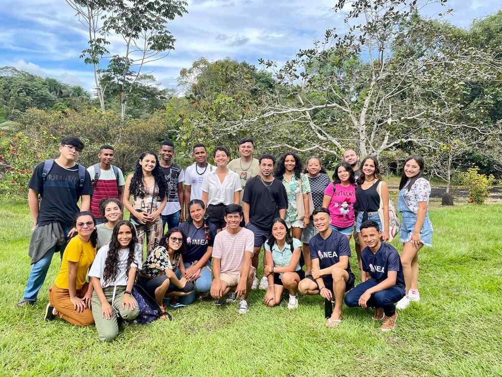 Grupo de pessoas reunidas ao ar livre. Elas sorriem para a foto em um gramado, e ao fundo há várias árvores