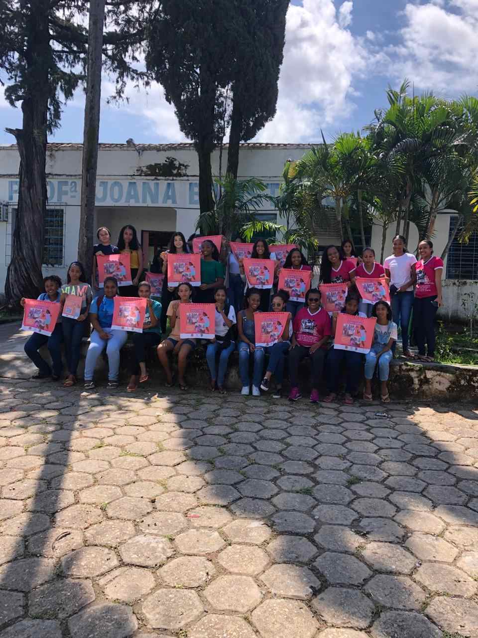 Grupo de meninas em um pátio sorrindo para a foto e segurando cartazes rosa