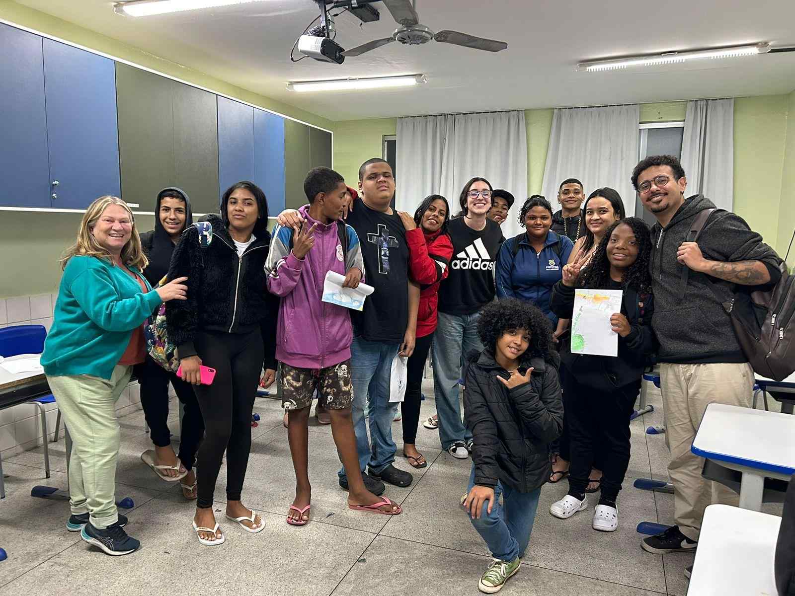 Grupo de pessoas diversas reunidas em uma sala de aula. As mesas estão afastadas, nos cantos da sala, e as pessoas estão reunidas no centro posando para a foto