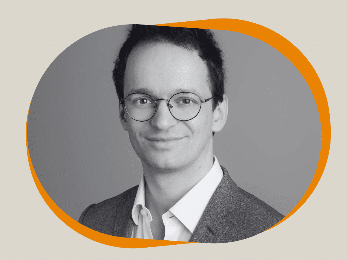 A smartly dressed man with glasses smiling to the camera