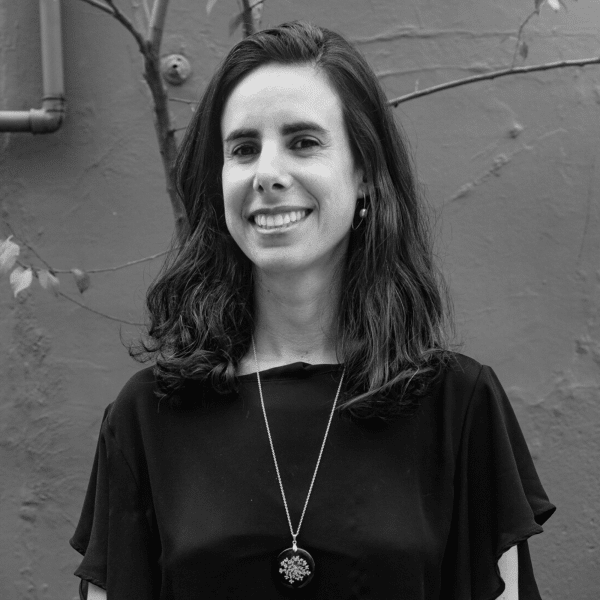 Black and white picture of Vitória Moraes. She is smiling, has medium wavy dark hair and is wearing a necklace and a blouse.