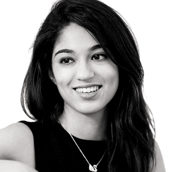 Photo of Prerna Aswani, Ashoka UK & Ireland Staff; black and white photo; person with dark long hair smiling and glancing to the left of the camera. Dressed in a dark form tank top and a metallic necklace. Background is white