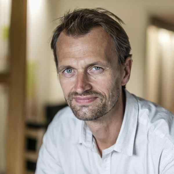 Portrait of Fellow Didier Ketels, he is wearing  a light blue shirt and smiling at the camera