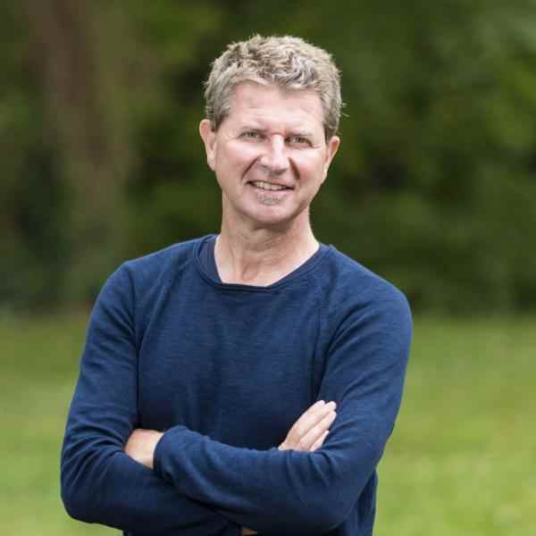 Portrait of Fellow Ignace Schops. He is wearing a long sleeve dark blue t-shirt and smiling at the camera. The background is out of focus greenery.