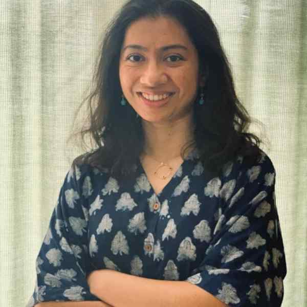 Person with blue and white top with crossed arms and shoulder length dark brown hair smiling at the camera. Background of light green curtains