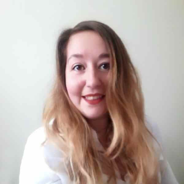Phot of a person with long half brown half light blonde hair smiling at the camera; dressed in a white top and background is a white wall