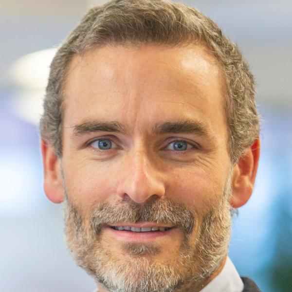 Photo of Ashoka staff member Loic Van Cutsem. Photo format is a classic headshot – person with short light brown / grey hair and a beard smiling at the camera. Background is blurred