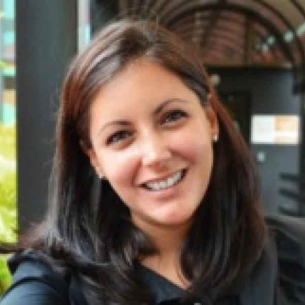 Photo of Lorena Garcia Duran, Director of DEI initiatives at Ashoka. Person with lighter skin and dark brown shoulder length hair smiling at the camera. Background of a covered walkway