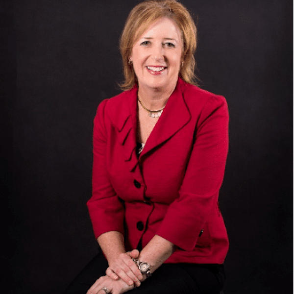 Photo of Leadership Group Member Lisa Davis. Person with shoulder light red / dark blonde hair smiling at the camera. Dressed in a professional red blouse and black pants. Background of black