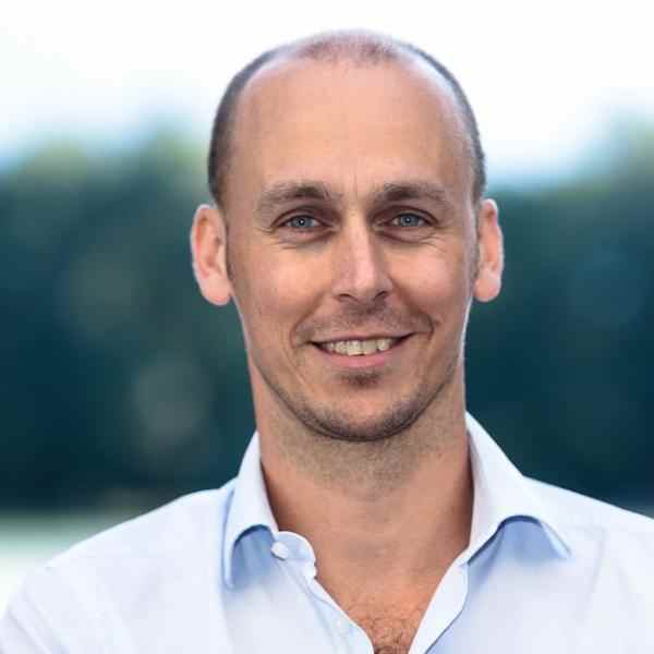 Photo of man in white shirt in front of green background 