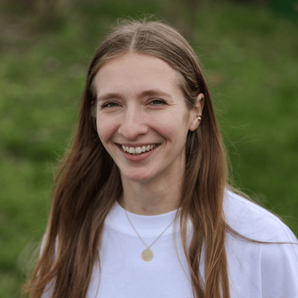Young woman in a white shirt, standing outside, smiling