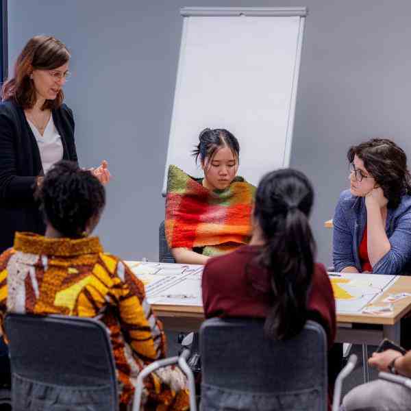 A group of young people sitting at the table and adult facilitator standing beside them