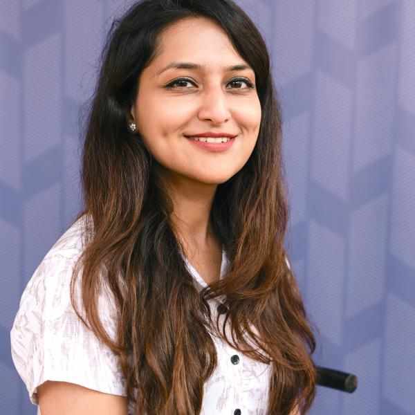 Person with long brown hair smiling at camera, dressed in white blouse. Background of blue
