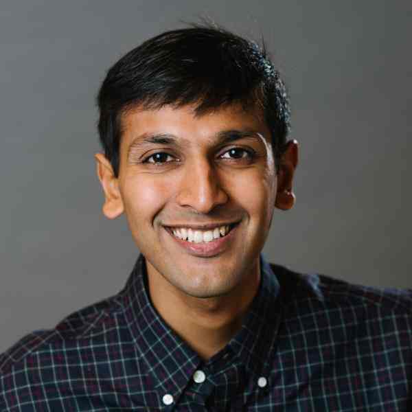 Photo of Indian man with short dark hair, wearing a black checked button-up shirt