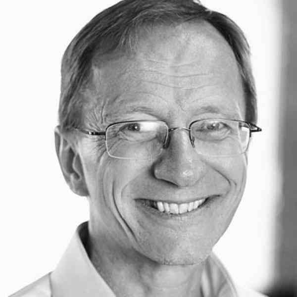 Black and white headshot of Bill Young, ASN member in Canada. Person with short dark hair and glasses smiling at the camera. Background a wall in a conference room