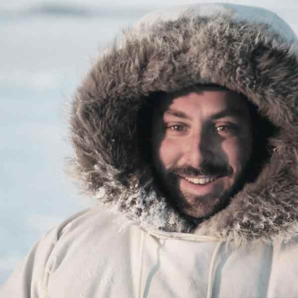 Profile picture of Ashoka Fellow Joel Heath. Person with a dark moustache and beard dressed in a white parka smiling at the camera; background is a field of snow