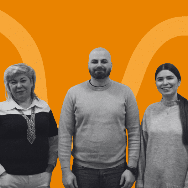 Grayscale photo of three people standing side by side, facing the camera. All three wear casual sweaters. The background is orange with abstract curved shapes