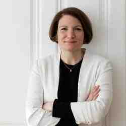 Photo of woman in white blazer in front of white door 