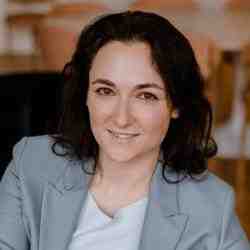 Photo of woman in dark hair and grey blazer smiling at the camera 