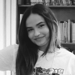 Foto em preto e branco de Carolina, jovem de cabelos longos e lisos que veste uma camiseta branca