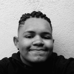 Foto em preto e branco de Vinicius, jovem negro de cabelo escuro e trançado. Ele veste um moletom preto e sorri levemente