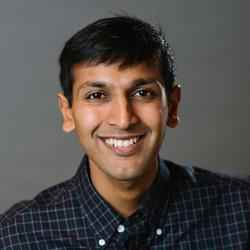 Photo of Indian man with short dark hair, wearing a black checked button-up shirt