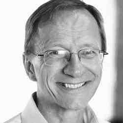 Black and white headshot of Bill Young, ASN member in Canada. Person with short dark hair and glasses smiling at the camera. Background a wall in a conference room
