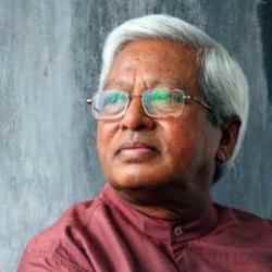 Photo of Sir Fzel Abed; person with red top and glasses looking right; background of a grey wall