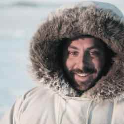 Profile picture of Ashoka Fellow Joel Heath. Person with a dark moustache and beard dressed in a white parka smiling at the camera; background is a field of snow