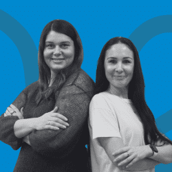 Two women standing back to back smiling